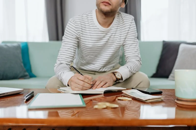 A man sitting on the couch writing with papers