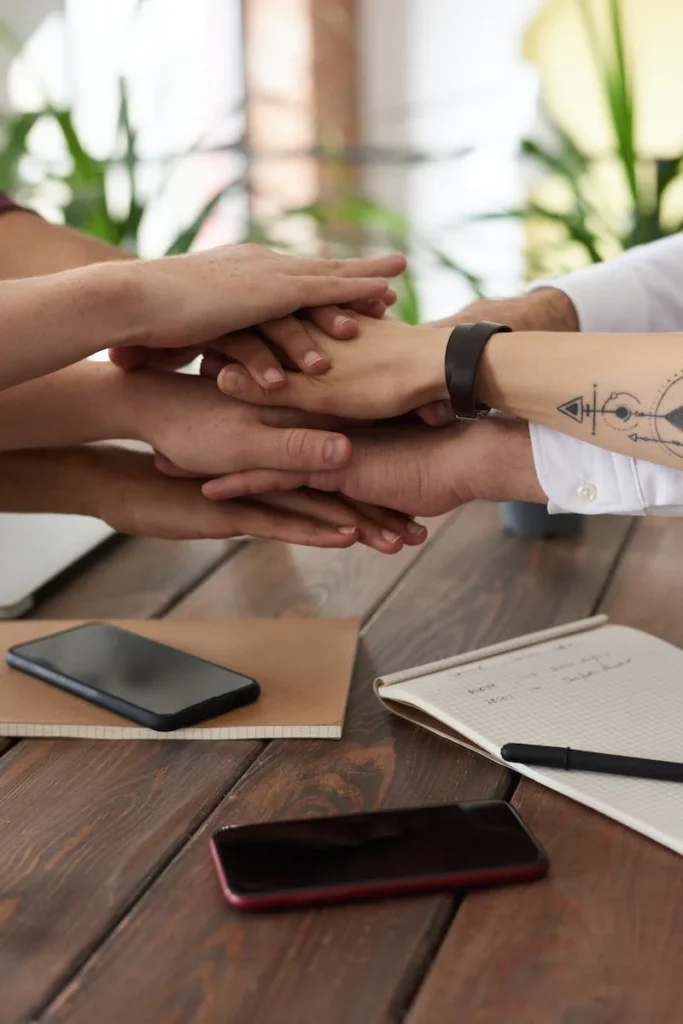 A group of people sitting at a table with their hands together.