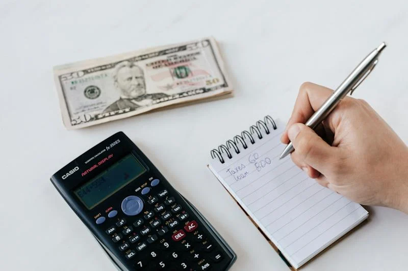 A person writing on paper next to a calculator and money.