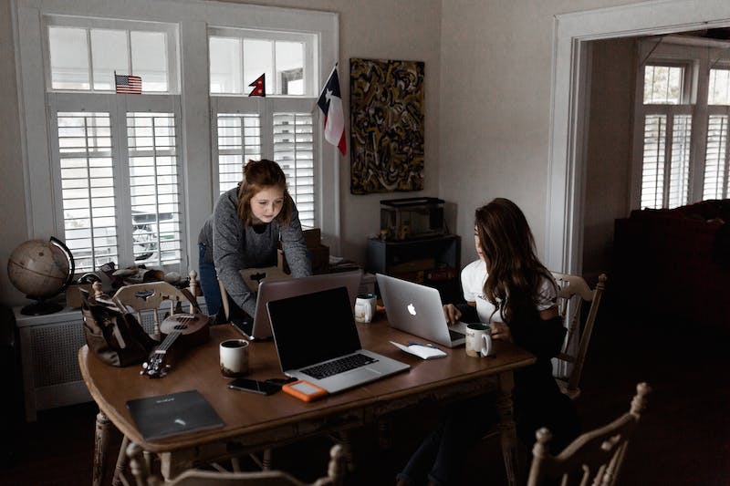 Two women sitting at a table with laptops.