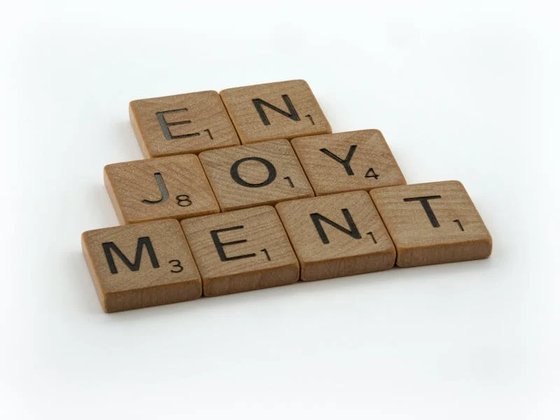 A wooden block that has the word enjoyment spelled out in scrabble tiles.