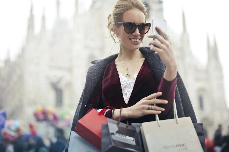 A woman holding shopping bags and looking at her phone.