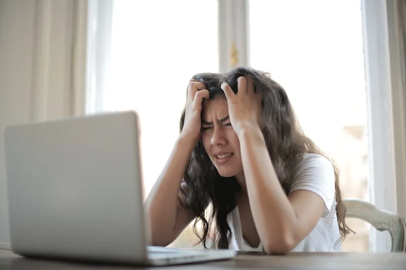 A woman sitting at the table with her hands on her head.