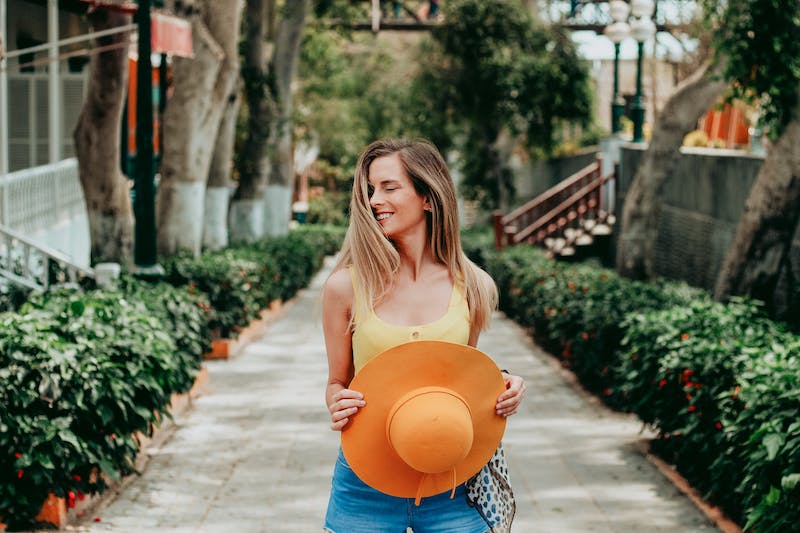 A woman holding an orange hat while standing on the sidewalk.