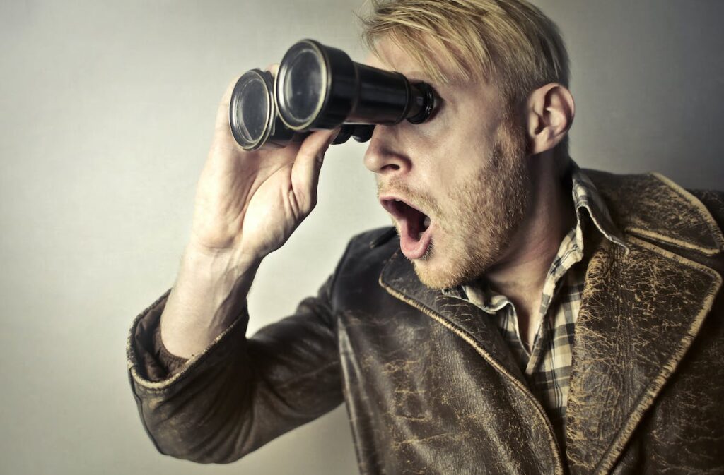 A man looking through binoculars with his mouth open.